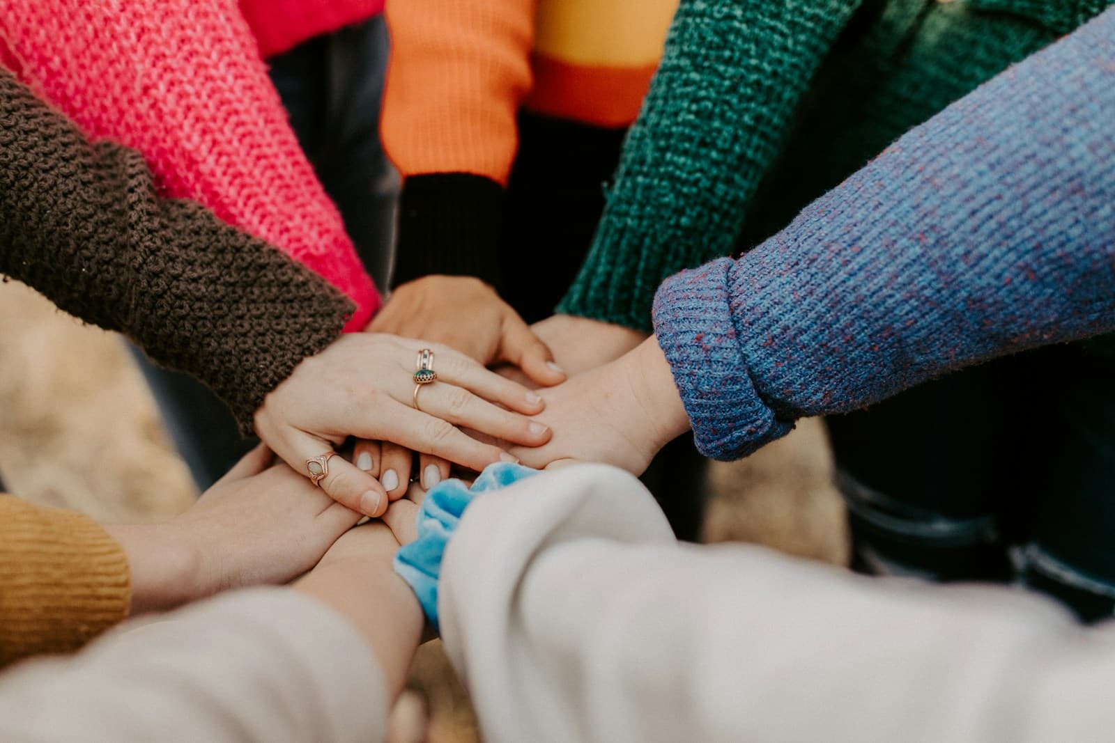 Several people in colourful knitted sweaters stacking their hands together
